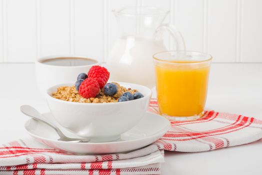 Bowl of granola and berries with coffee and orange juice.