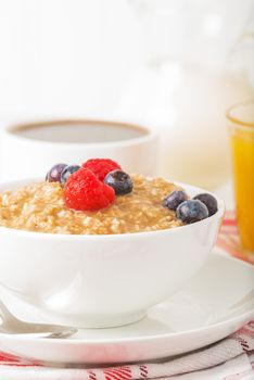 Bowl of hot oatmeal and fresh berries with coffee and orange juice.