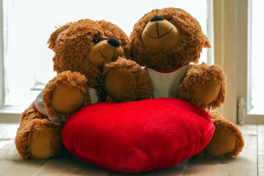 Two teddy bears sitting on the table hugging each other