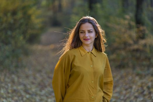 Yellow afternoon. Beautiful teenager girl posing in yellow shirt in a forest. She looks thoughtfully away. Her hair is backlit by sun. Action takes place in an afternoon autumn forest.