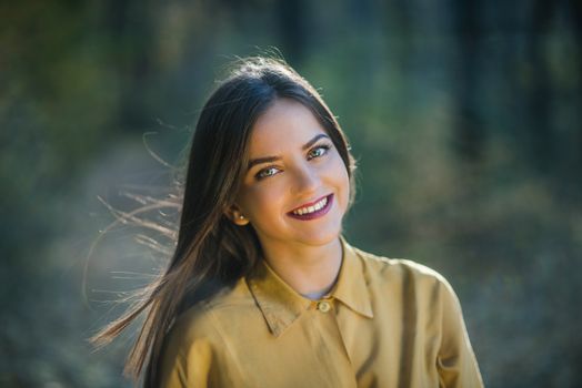 Portrait of smiling girl with bright eyes. Portrait of a beatiful smiling teenager girl with bright eyes wearing yellow shirt in the woods. Warm autumn afternoon.