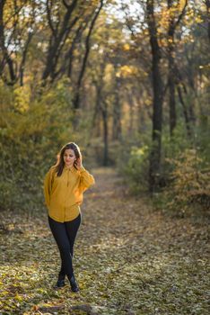 Thoughtful girl in the autumn forest. A nice girl in stretch jeans and yellow shirt is posing in a forest. She does not looking into camera. Action takes place in an afternoon autumn forest full of yellow leaves.