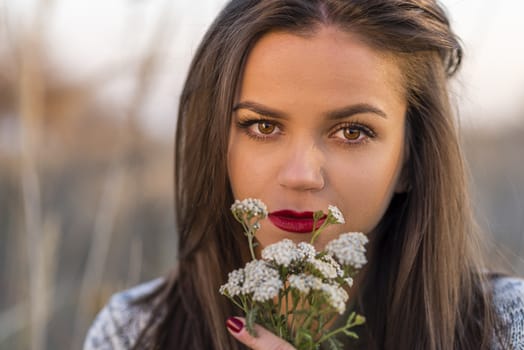 Sad autumn look. Portrait of a nice teenager girl holding small bouquet in a autumn field. Girl has brown eyes and hair and red lips.