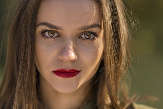 A close-up portrait of a teenage girl with a cold look. Girl has red lips and brown eyes.