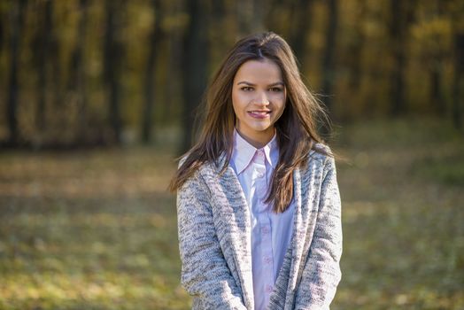 Smiling girl is posing in a autumn forest in a warm knitted blouse. Action takes place in an autumn afternoon.