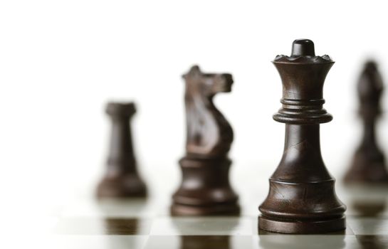 Horizontal image of a chess game with focus on the queen and a blurry pieces over white background, Copy space on the left side. Concept of corporate strategic management or planning or business intelligence.