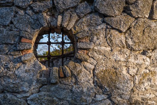 Round shaped window with a lattice in a stone fence. Window in a fence.