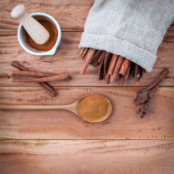 Composition of cinnamon stick in hemp sack and cinnamon powder in white mortar and  cinnamon powder in wooden spoon on rustic old wooden background .