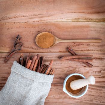 Composition of cinnamon stick in hemp sack and cinnamon powder in white mortar and  cinnamon powder in wooden spoon on rustic old wooden background .