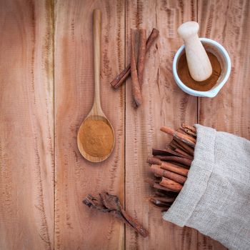 Composition of cinnamon stick in hemp sack and cinnamon powder in white mortar and  cinnamon powder in wooden spoon on rustic old wooden background .