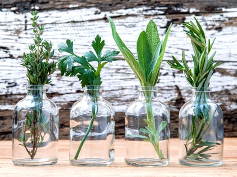 Bottle of essential oil with herbs rosemary, sage,parsley  and thyme  set up on old wooden background .