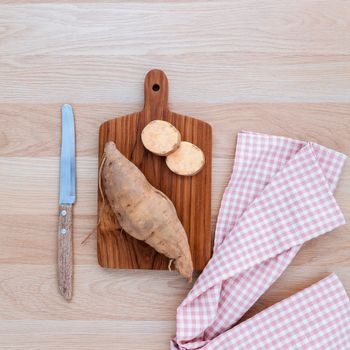 Organic sweet potatoes with cutting board and knife on rustic wood table.