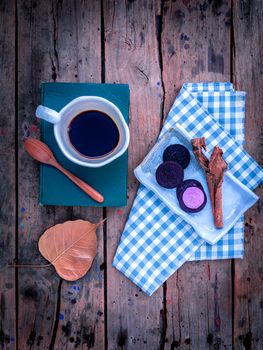 Cup of coffee  on textbook with black biscuits and cinnamon on rustic wooden table.