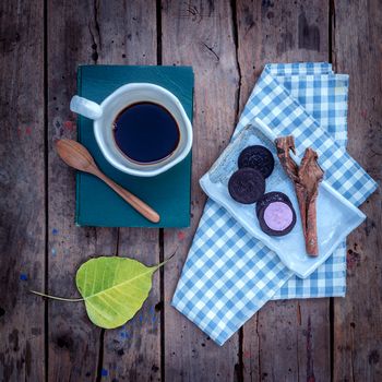 Cup of coffee  on textbook with black biscuits and cinnamon on rustic wooden table.