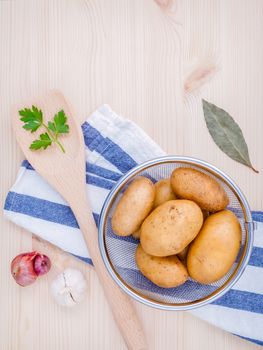 Fresh organic potatoes in basket with herbs garlic,shallot ,parsley and bay leaves on rustic wooden table. Preparation for cooking.