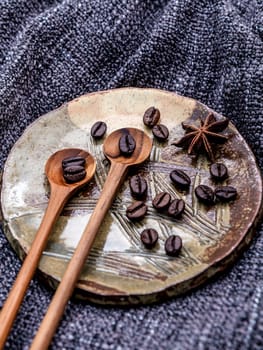 Coffee beans and star anise in ceramic plate with wooden spoons on dark fabric .