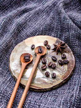 Coffee beans and star anise in ceramic plate with wooden spoons on dark fabric .