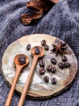 Coffee beans and star anise in ceramic plate with wooden spoons on dark fabric .