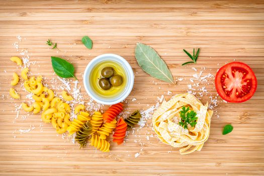 Italian food concept pasta with vegetables olive oil and spices herbs parsley , basil ,bay leaves and rosemary set up with white cheese on wooden background.