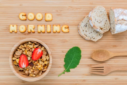 Good morning concept - Cereal in wooden bowl with strawberry and wooden spoon set up on wooden background.