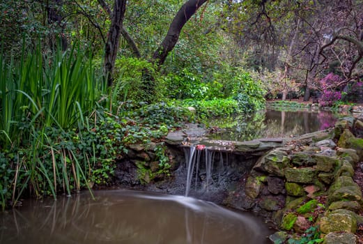 Peaceful stream and waterfall in spring with foliage and blooming trees.