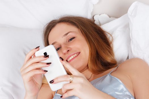 Portrait of a happy woman in her lovely bedroom texting