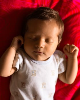 Newborn boy sleeping peacefully on a red background