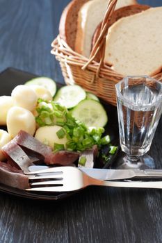 Black plate with herring and potatoes near glass of vodka