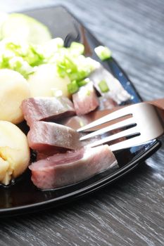 Black plate with herring and potatoes near fork