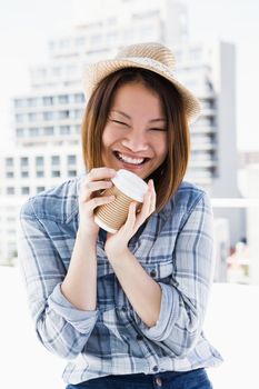 Young woman holding disposable cup and smiling outdoors