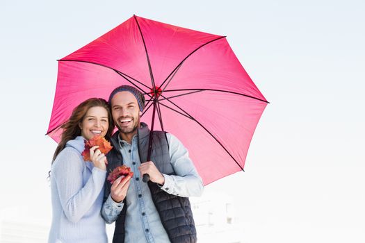 Happy young couple holding umbrella and maple leaves outdoors