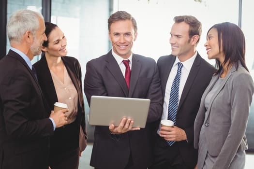 Businesspeople standing together with a laptop in office