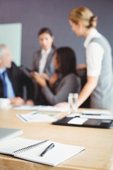 Organizer with pen on table in conference room and businesspeople interacting in background