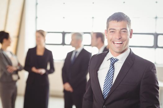 Portrait of excited young businessman with people discussing in background