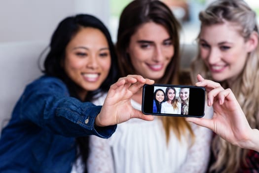 Happy beautiful young female friends taking selfie with mobile phone at home