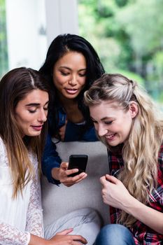 Close-up of happy young female friends looking in mobile phone at living room