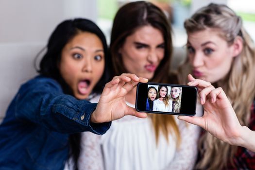 Beautiful young female friends taking selfie with mobile phone at home