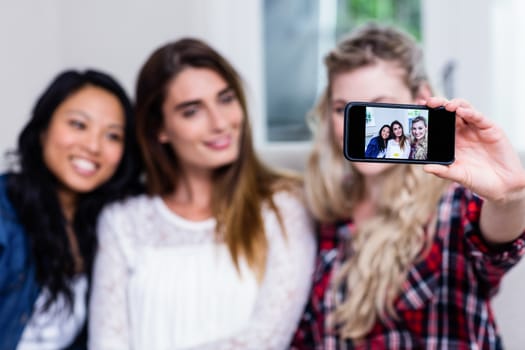 Happy young female friends taking selfie with smart phone at home