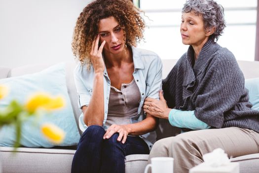 Mother comforting sad daughter sitting on sofa at home