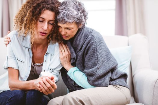 Mother comforting tensed daughter sitting on sofa at home