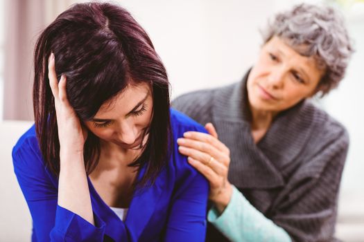 Mother comforting sad daughter sitting on sofa at home