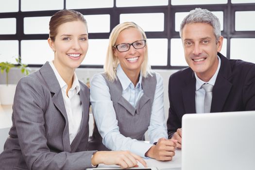 Portrait of happy business people with laptop at desk during meeting