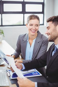 Smiling business people discussing over documents at computer desk in office