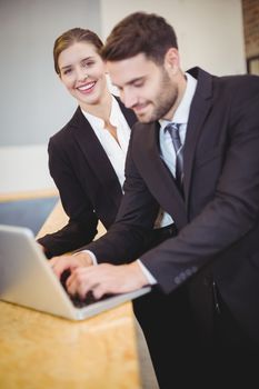 Happy business people using laptop by counter at office