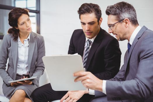 Business professionals holding documents on clipboard while sitting on sofa in office