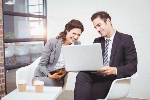 Cheerful business people using technology while discussing at office