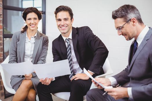 Cheerful business professionals holding documents while sitting on sofa in office