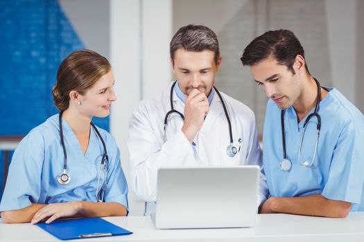 Doctors using laptop while standing at desk in hospital