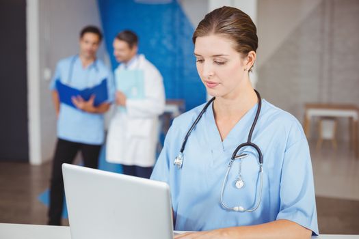 Female doctor working on laptop with colleagues discussing on background