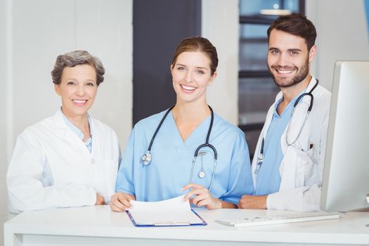 Portrait of smiling doctor team standing at computer desk in hospital